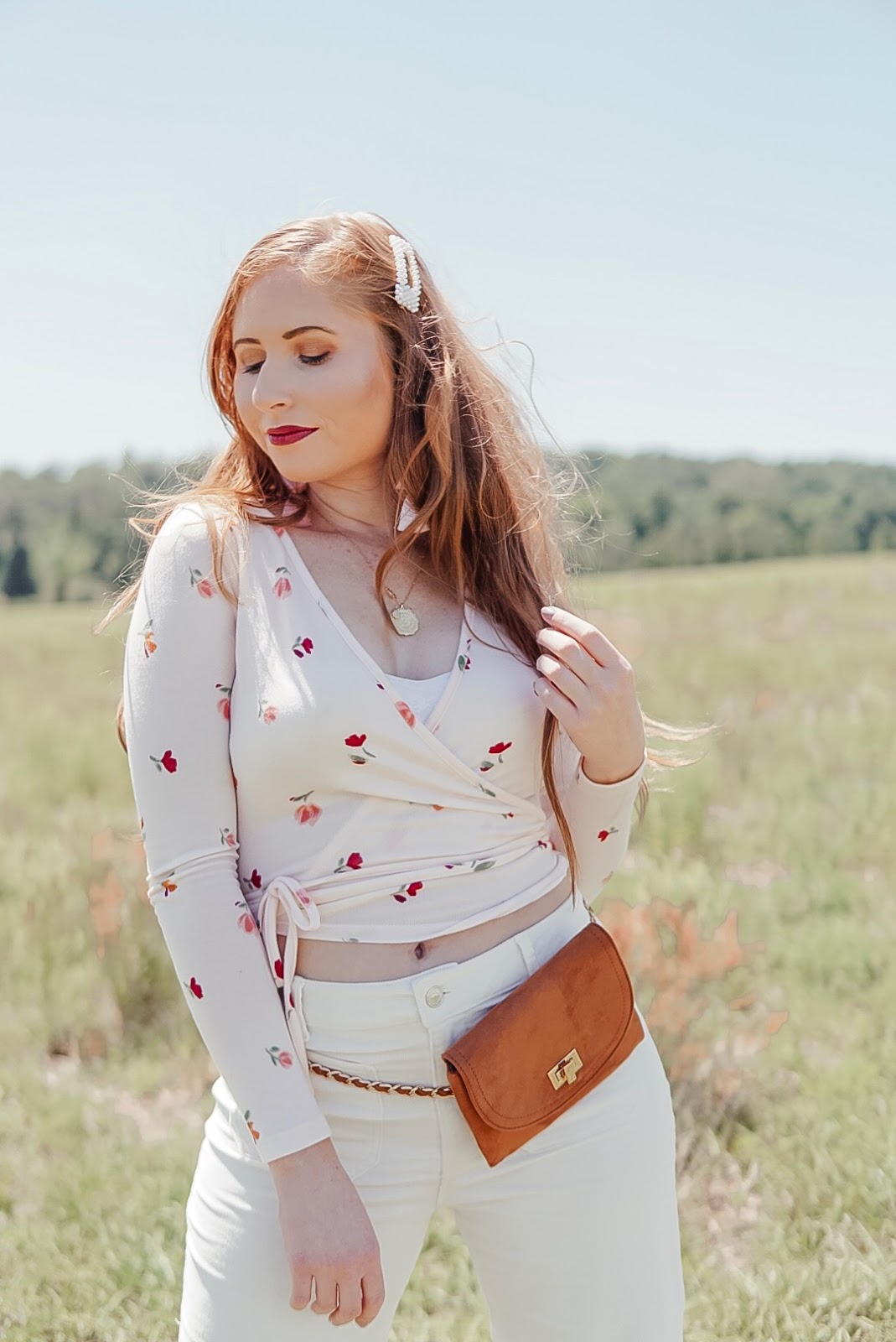 tampa blogger amanda burrows of affordable by amanda is wearing a florap wrap top and white corduroy jeans out in a wildflower field. she is wearing long extensions from barefoot blonde extensions in the color chestnut.