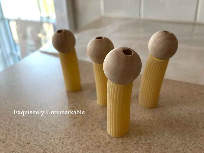 Rigatoni pasta with wooden beads for heads lined up on a table