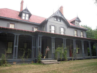 Gray Queen Anne-style house with red roof, porch all along the front