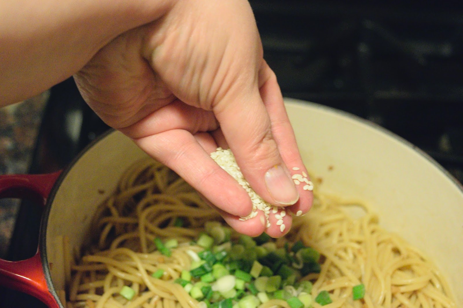 Chopped green onions and sesame seeds being added to the pot with the noodles.