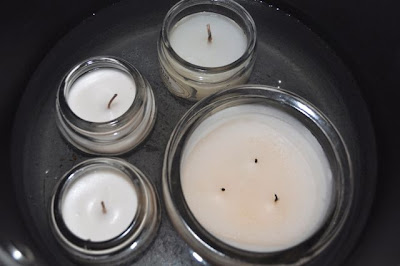glass candles with white wax inside pot with water inside