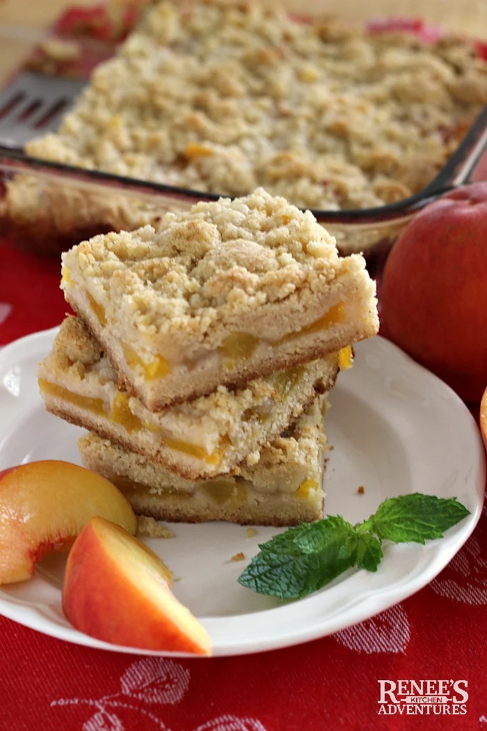 Easy Peach Crumb Bars stacked on a plate with pan of Easy Peach Crumb Bars in background