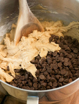 mixer bowl full of brown sugar dough and lots of chocolate chips with wooden spoon