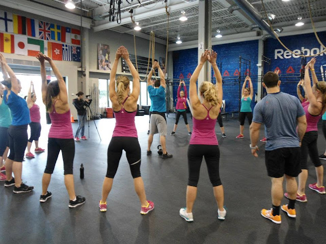 image of Fitfluential bloggers stretching with arms overhead in a circle at the Reebok CrossFit ONE facility before a workout