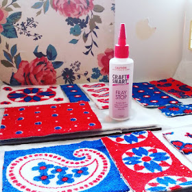 Selection of miniature rugs in retro designs of white, teal and red laid out next to a bottle of fray stop