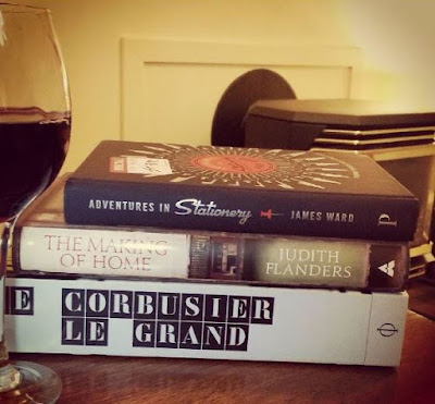 Three books in a pile next to a glass of red wine.