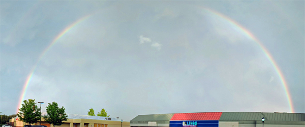 image of a rainbow arcing across a stormy sky, above a strip mall