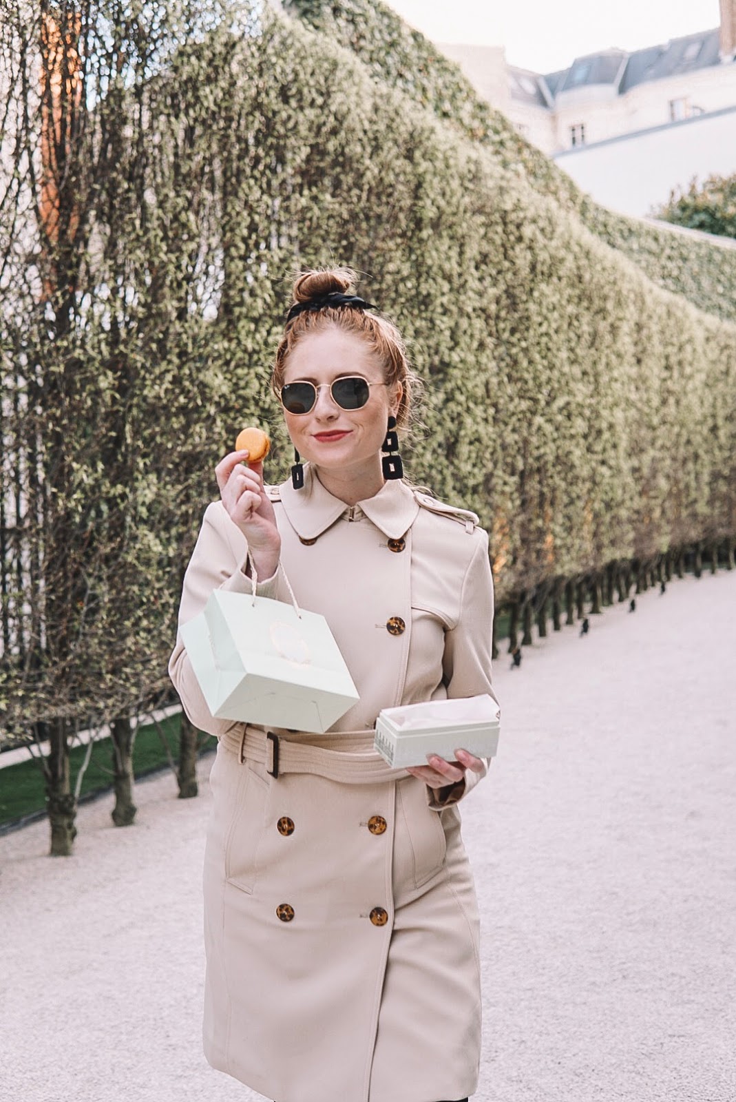 tampa blogger amanda burrows of affordable by amanda wears a tan trench coat while snacking on macaroons from laduree in paris, france.