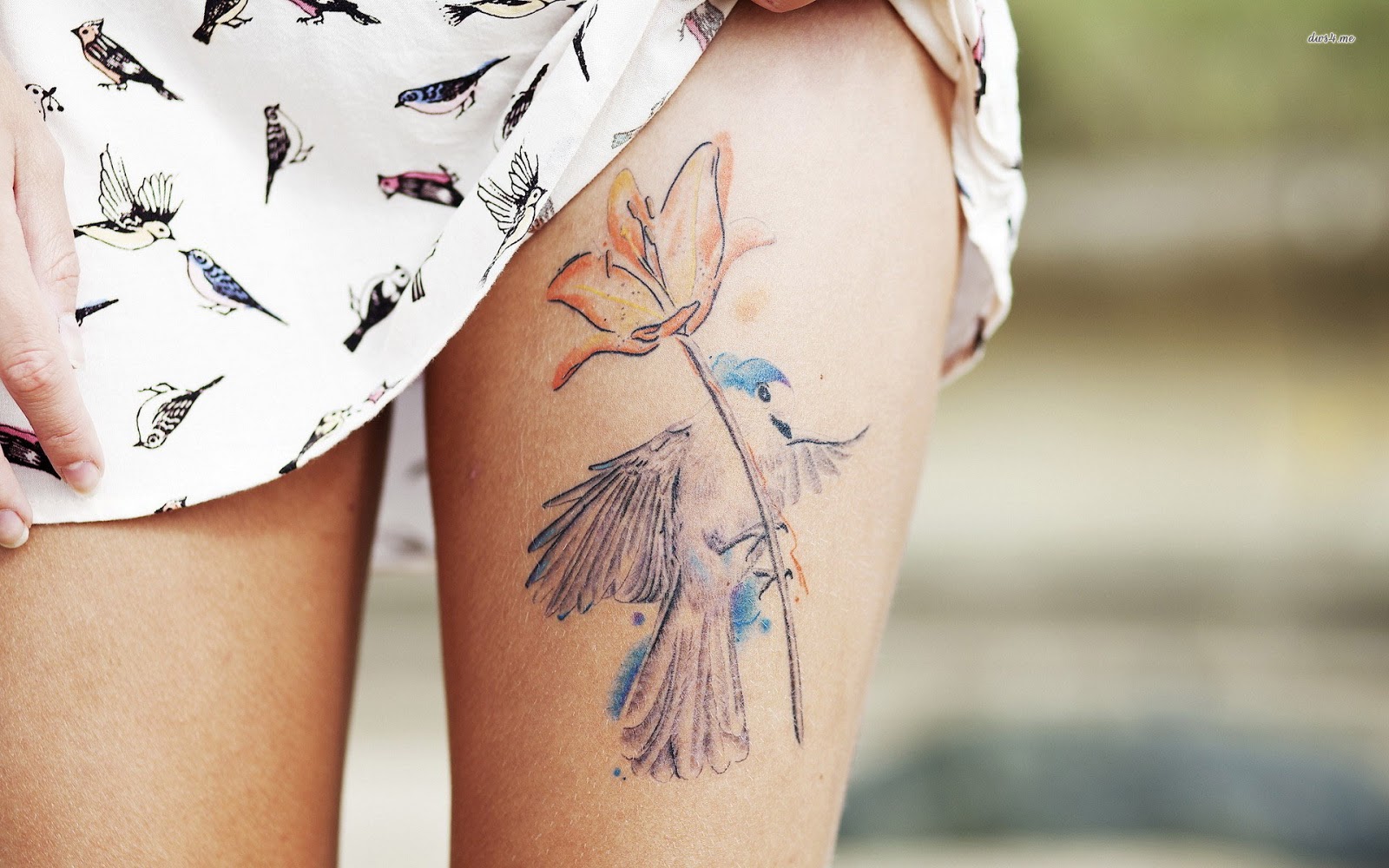 chica nos enseña su tatuaje en la parte superior del muslo de un colibri y ina amapola