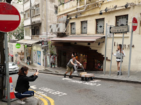 man pushes a cart through the scene as a woman tries to photograph another woman