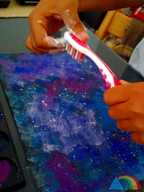 Salpicando gotas de pintura blanca con un cepillo de dientes para simular las estrellas