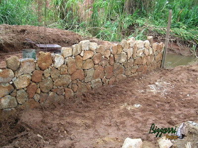 Construção do muro de pedra com pedra bruta para a base da construção da ponte de concreto na entrada da empresa em Atibaia-SP.