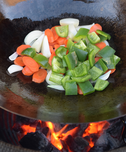 Stir frying veggies in a wok over hot lump charcoal in a kamado style grill.