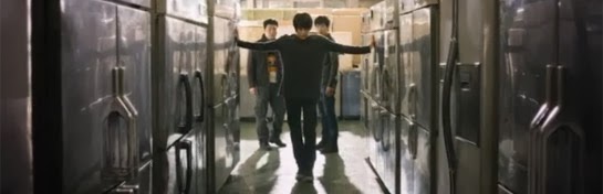Kim Joon walks down a line of freezers as Choon Dong and Yang Soo, played by Lee Joon Hyuk 이준혁, watch.