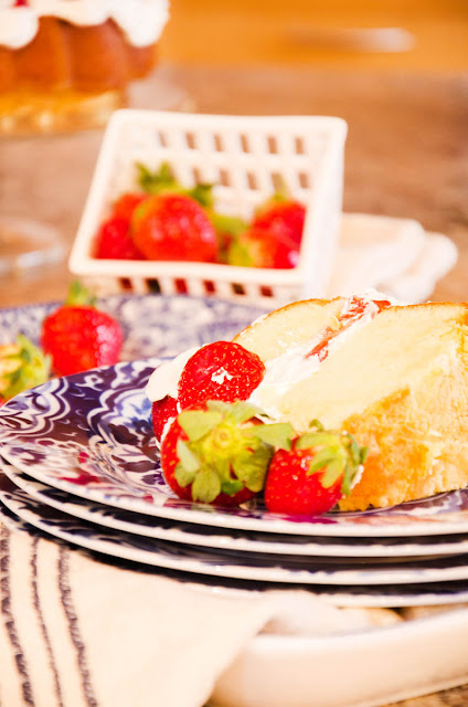 A slice of strawberry pound shortcake garnished with fresh strawberries placed on a blue and white plate with a basket of strawberries in the background.