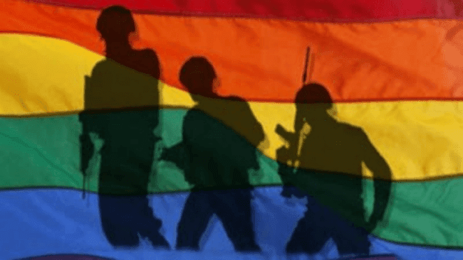 Military members shadow behind a rainbow flag.
