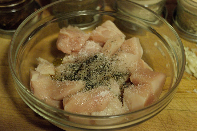 Salt and pepper on the diced chicken in a bowl.