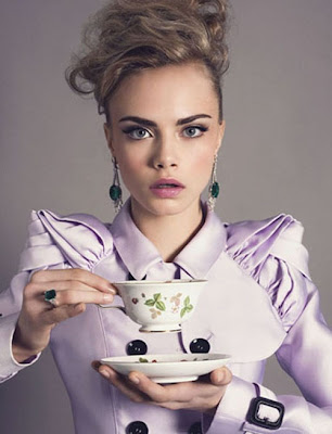 model Cara Delevingne posing in a lilac pastel coat, preparing to sip tea.