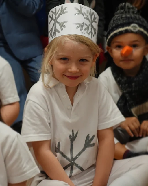 A 5 year old with a white t-shirt with a snowflake on and a white and silver snowflake hat