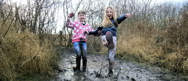 two girls splashing in muddy puddle wellies