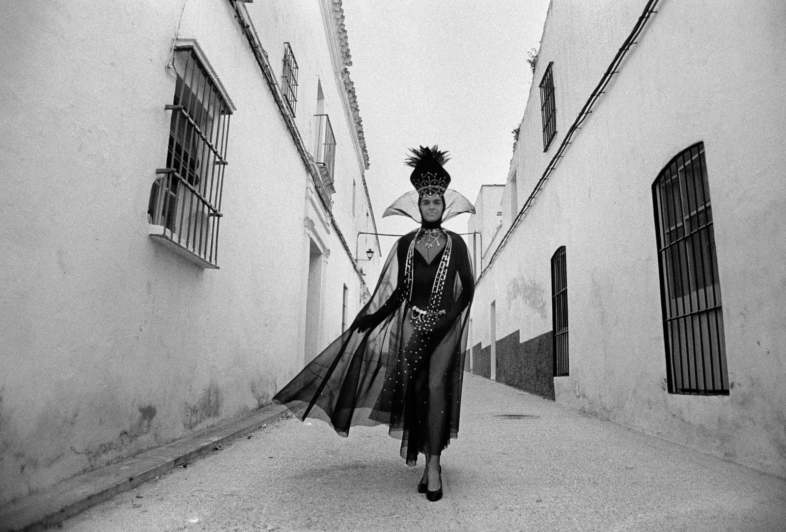 A  person dressed very dramatic in black and heels in the middle of a typical andalusian white street
