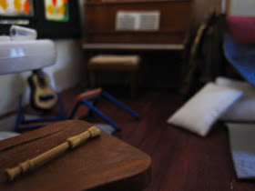 Modern dolls' house miniature post-party scene showing a piano, guitar and recorder, plus a broken chair.