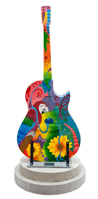 outdoor art display in downtown Orillia featuring painted guitars - this guitar has a design of sunflowers with a large parrot