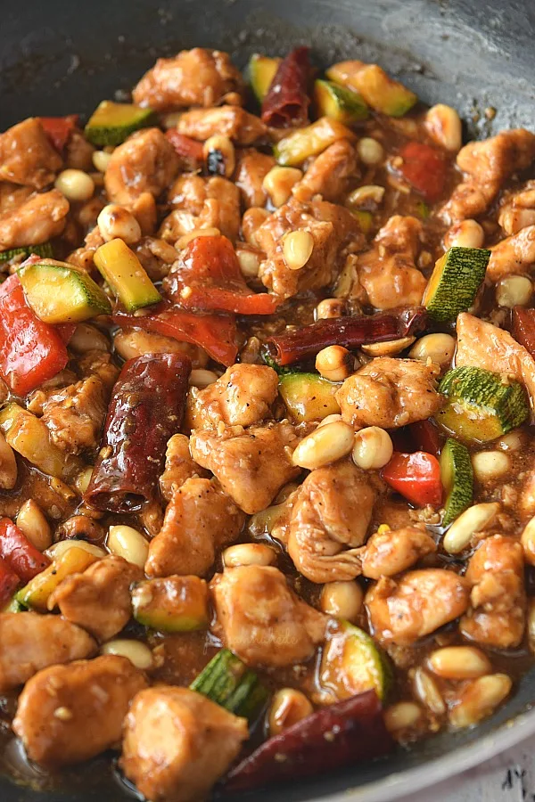 a pan with delicious kung pao chicken tossed in sauces along with peanuts,zucchini and bell peppers