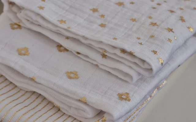 3 white muslins folded up with a different pattern in gold metallic on each one (stripes, diamonds and stars)
