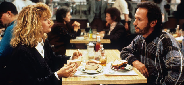 Meg Ryan and Billy Crystal in When Harry Met Sally (1989). Image shows Sally and Harry seated in Katz's Delicatessen after the . She is holding a sandwich after just finishing faking an orgasm while he looks on embarrassed.