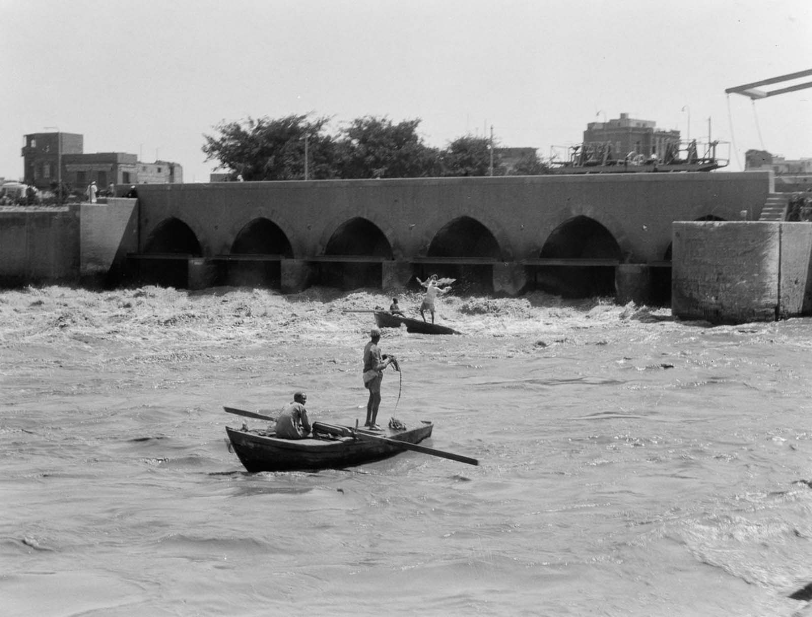 Fishermen cast their nets into the current beneath a bridge. 1934.