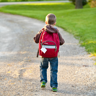 Picture of a boy wearing a backpack walking down a gravel road