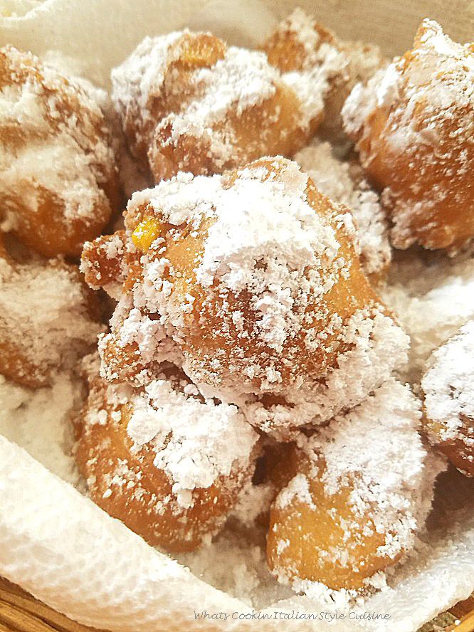these are an old fashioned corn fritter shaped like donut holes with powdered sugar on top in a wicker basket lined with white paper towels. These corn fritters are eaten warm rolled in sugar.