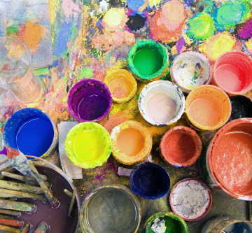 open used multicolored cans of paint and brushes sitting on painted abstract canvas