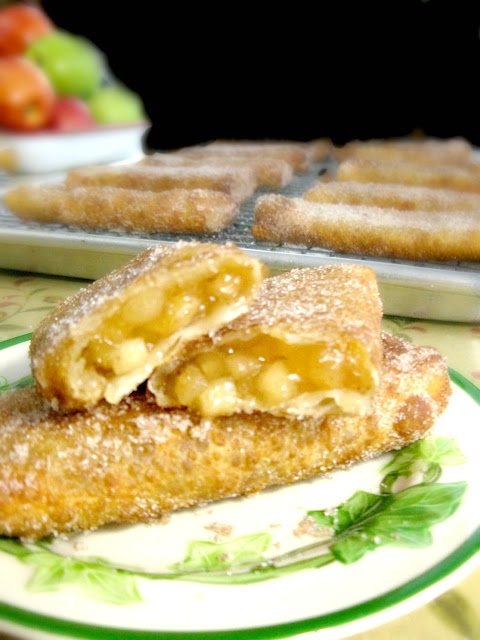 This is a photo showing two fried apple pies on a plate stacked on top of each other. The top pie is broken in half, showing the filling. 