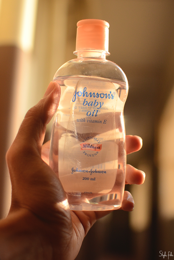 Image of a woman's hands holding a Johnson's Baby Oil bottle against a brown background in sunlight