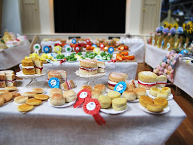 Baking with prize ribbons on a stall in a one-twelfth scale scene of a CWI wartime fundraising fete in a hall.