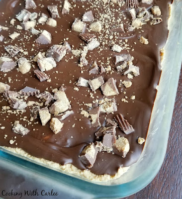Peanut butter, graham crackers and chocolate come together in a fun no bake bar. These fun treats are sure to get rave reviews everywhere you take them. They are so easy to put together they are likely to become your new go to dessert! Corner of pan showing the edge of the peanut butter layer covered in chocolate and lots of chopped peanut butter cups