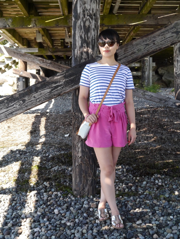 Striped tee worn with fuchsia silk shorts, metallic leather sandals, and a small but colourful crossbody bag and cat-eye shades.