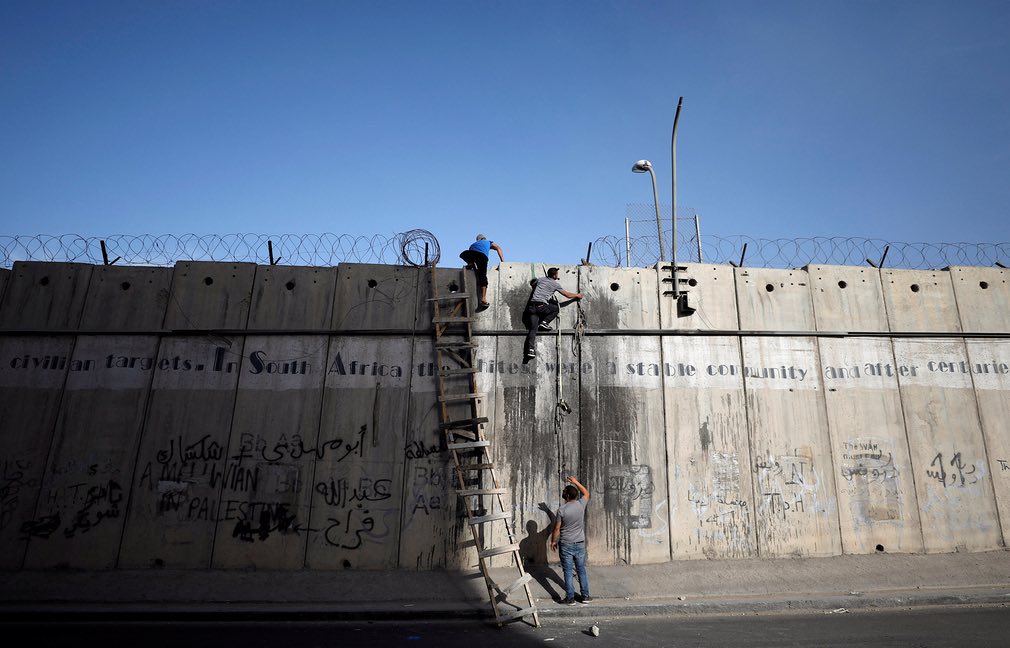 Palestinians climb over a section of the Israeli barrier Tears of Gaza
