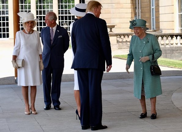 Melania Trump is wearing a custom white crepe dress with navy details by Italian fashion house, Dolce & Gabbana. Queen Elizabeth