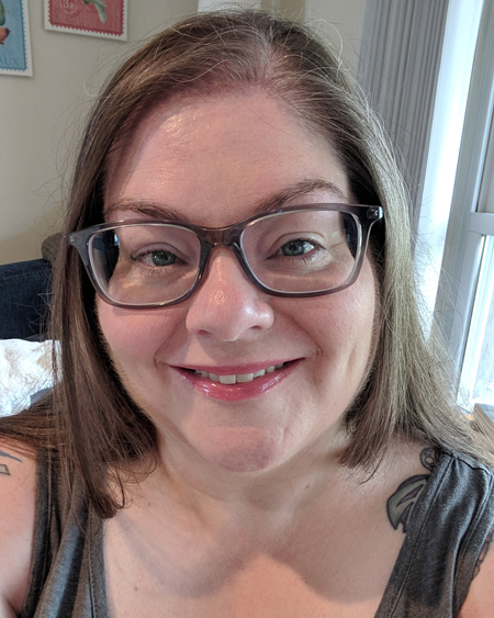 image of me from the shoulders up, wearing grey-framed glasses and a grey tank top, smiling
