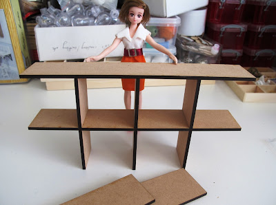 Dry-built modern dolls' house miniature laser-cut 'pidgeon' hole kit  with dolls' house doll for scale.
