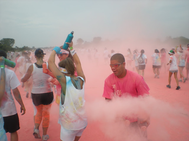 A man throws colored powder around while participants run past during a color run