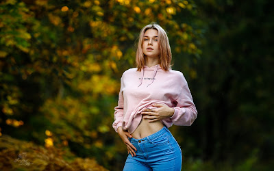 Chica rubia con vaqueros y sudadera rosa en el bosque