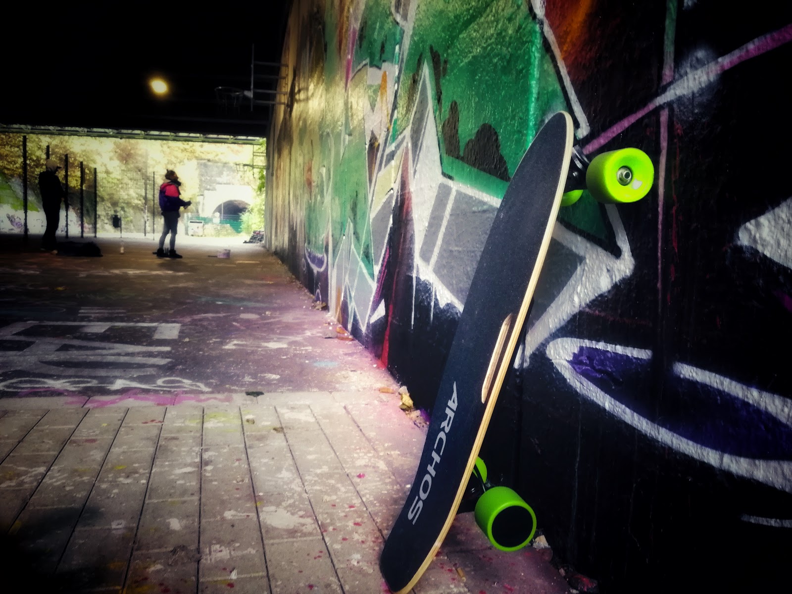 ARCHOS SK8 an einer Graffiti Wall angelehnt im Hintergrund sieht man Sprayer