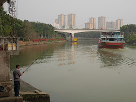 man fishing as a ship travels down the Jiangmen Waterway