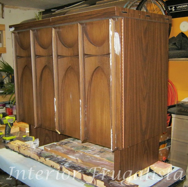 A mid-century modern sewing cabinet with damaged and missing trim on one door before furniture repair.