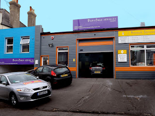 Photograph showing two fascias over workshop garage shop front. The fasicas are purple in colour with white text showing contact details for the workshop.