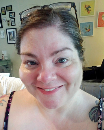 image of me from the shoulders up, wearing a tank top, with my hair up and my glasses perched on top of my head, smiling, with no makeup on and clear skin